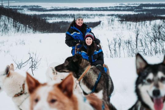 Two guests dog sledding with happy huskies