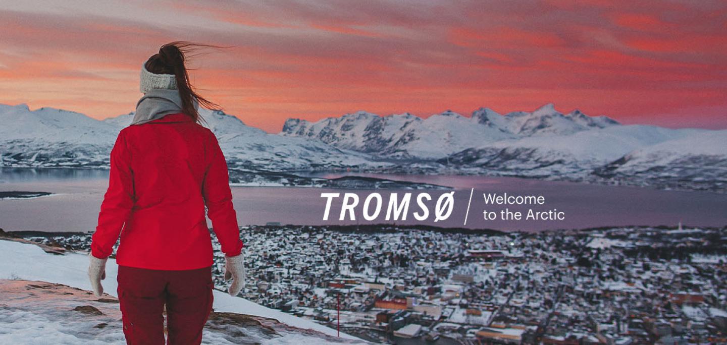 Woman hiking with a view of Tromsø during sunset with Visit Tromsø logo