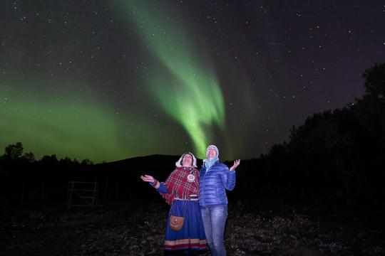 Sami lady and guest admiring the Northern lights together